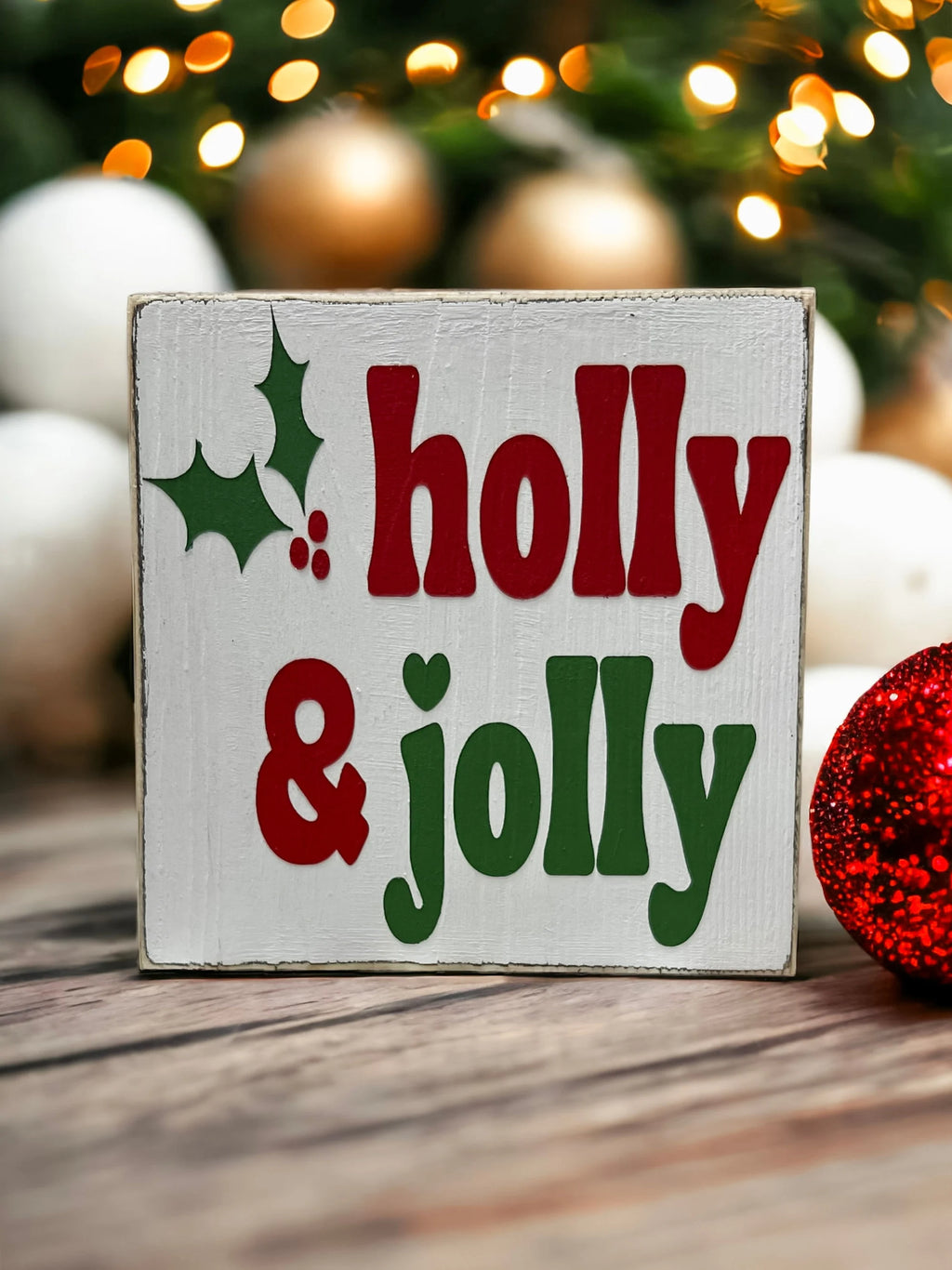 Holly & Jolly wood sign close-up with pine cone and fairy lights