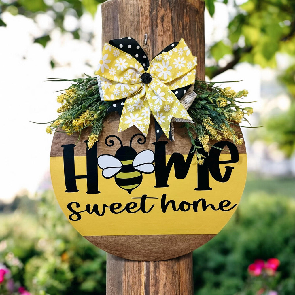Home Sweet Home bee round pine door hanger yellow and walnut two-tone with daisy polka dot bow and wildflower greenery on rustic wood post in garden with red roses hero shot