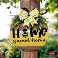 Home Sweet Home bee round pine door hanger yellow and walnut two-tone with daisy polka dot bow and wildflower greenery on rustic wood post in garden with red roses hero shot