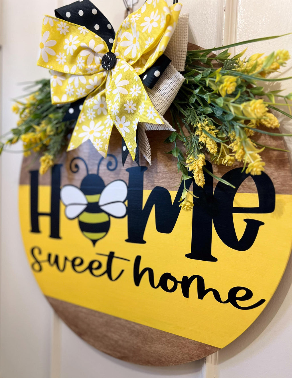Home Sweet Home bee round pine door hanger yellow and walnut two-tone with daisy polka dot bow and wildflower greenery on rustic wood post in garden with red roses side angle