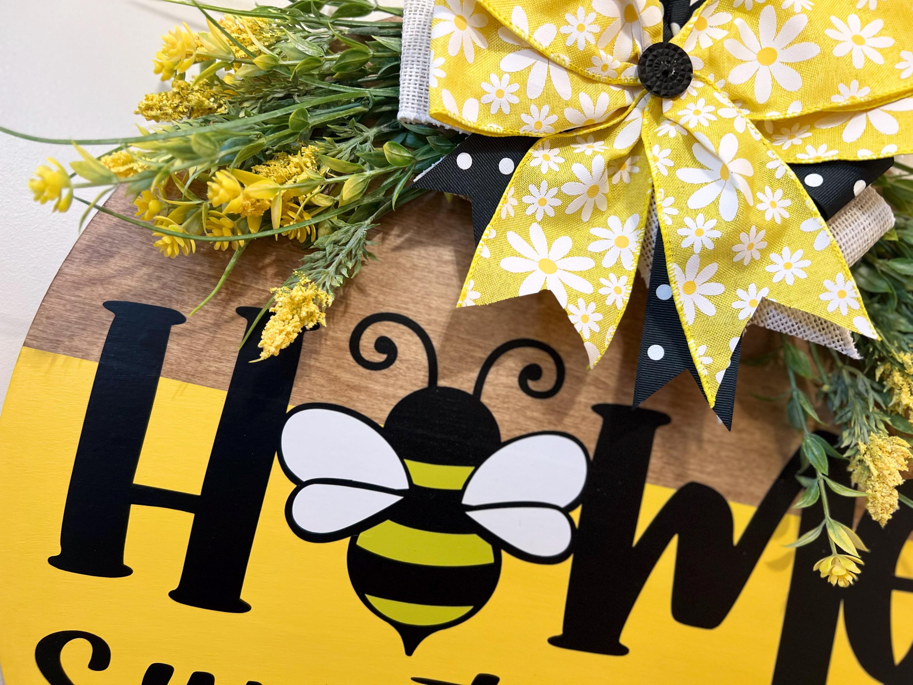 Home Sweet Home bee round pine door hanger yellow and walnut two-tone with daisy polka dot bow and wildflower greenery on rustic wood post in garden with red roses angled view
