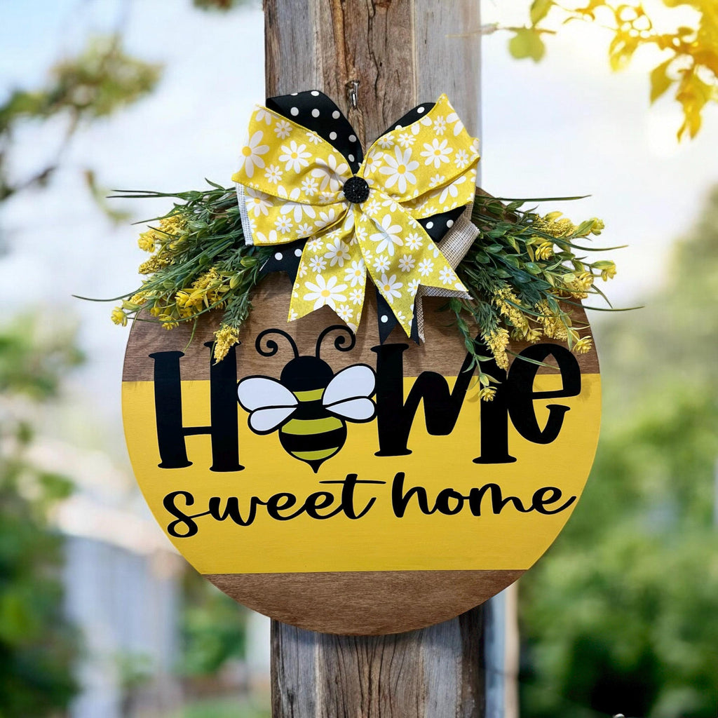Home Sweet Home bee round pine door hanger yellow and walnut two-tone with daisy polka dot bow and wildflower greenery close up of bee graphic and bow detail on white background