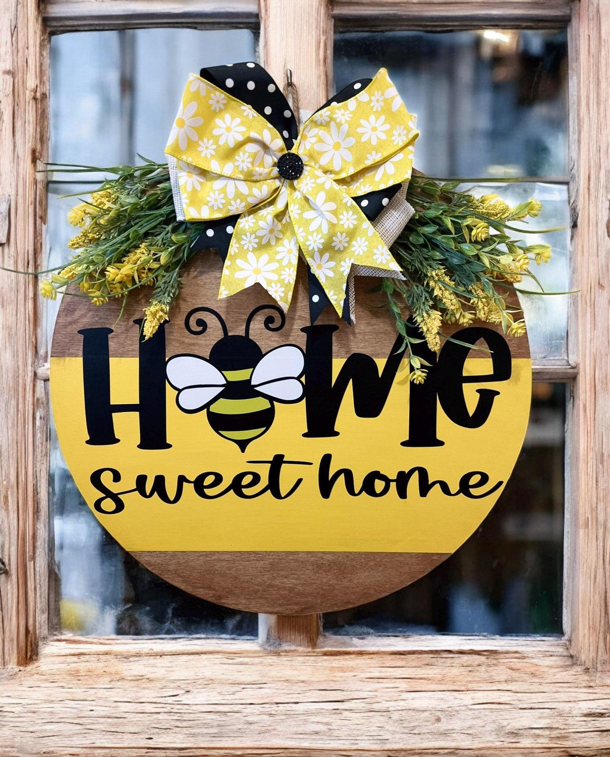 Home Sweet Home bee round pine door hanger yellow and walnut two-tone with daisy polka dot bow and wildflower greenery on rustic wood post in garden with bokeh flowers warm light