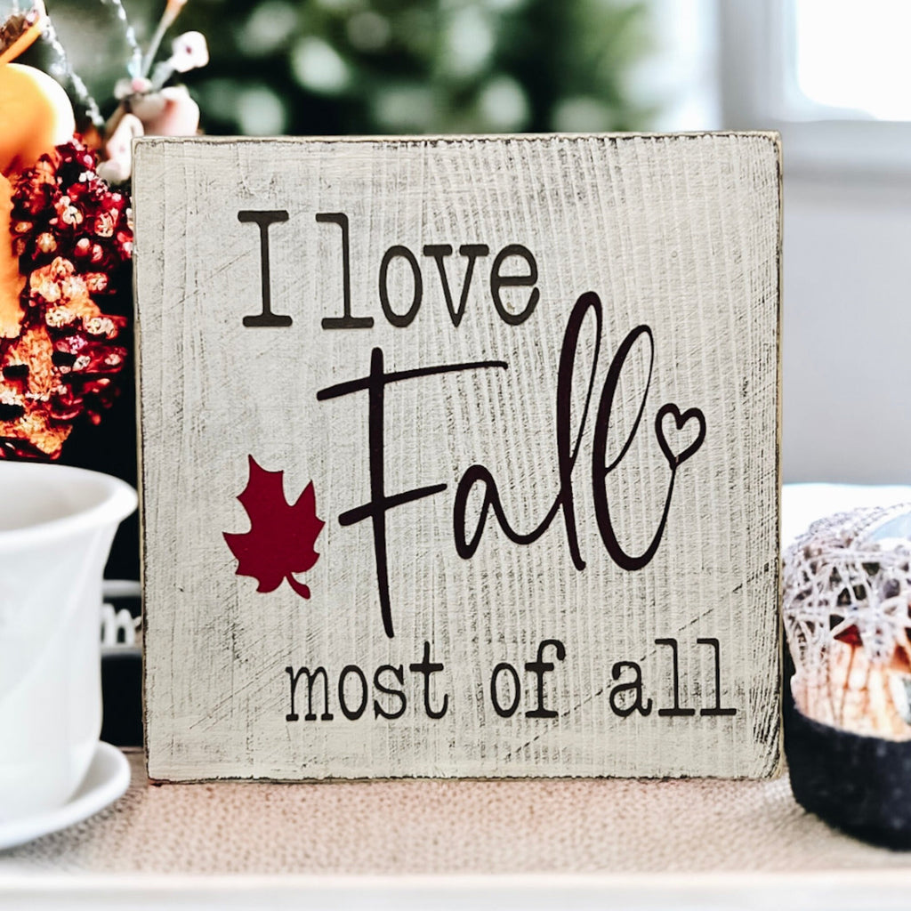 I Love Fall Most of All distressed off-white wood block sign with black lettering and burgundy maple leaf on round wood tray with copper pot dried botanicals and orange pumpkins