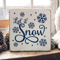 Let It Snow navy wood block sign on snowy windowsill with pine cones and knit scarf