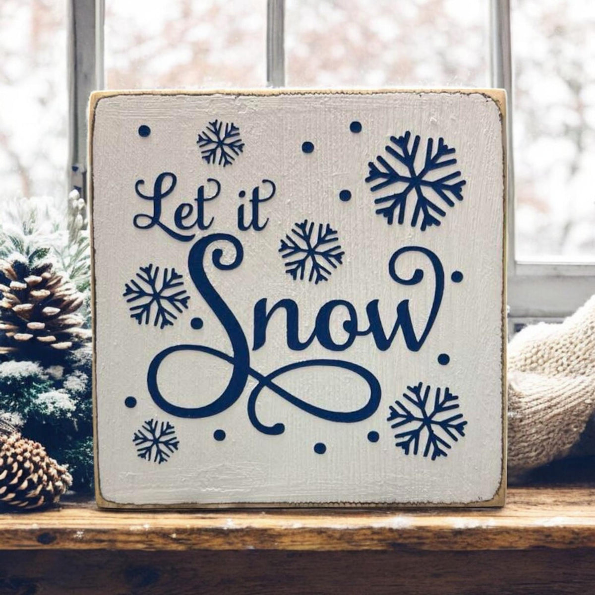 Let It Snow sign on rustic wood surface with pine cones and mini Christmas trees