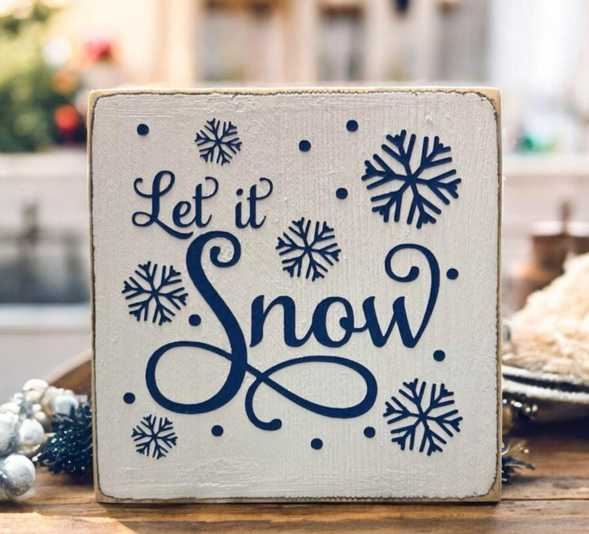 Let It Snow sign on white cake stand with holiday garland and ornaments