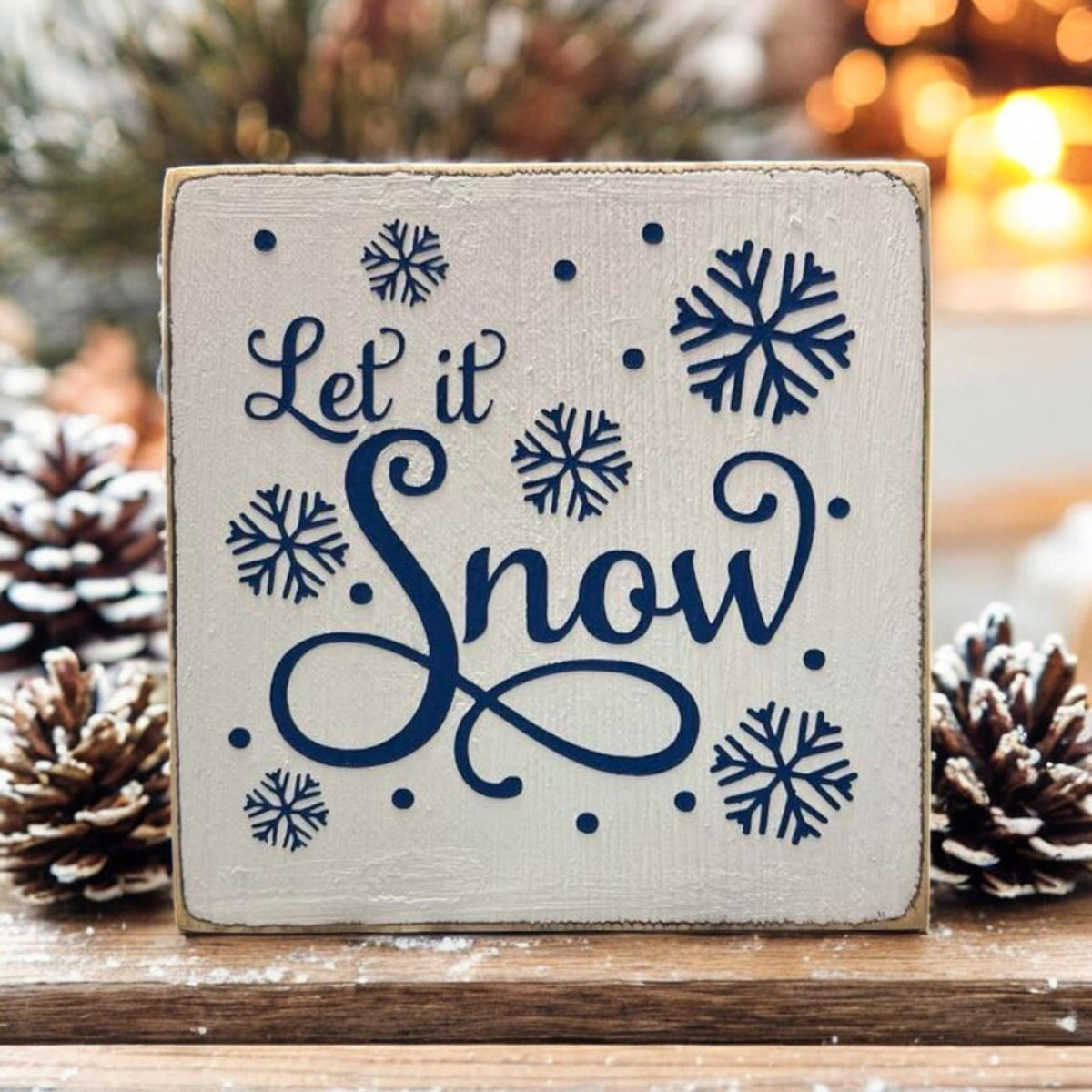 Let It Snow sign on snowy windowsill with frosted pine cones and knit glove