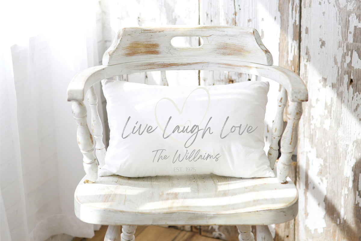Personalized Live Laugh Love lumbar pillow on white distressed wood surface close up of heart and name