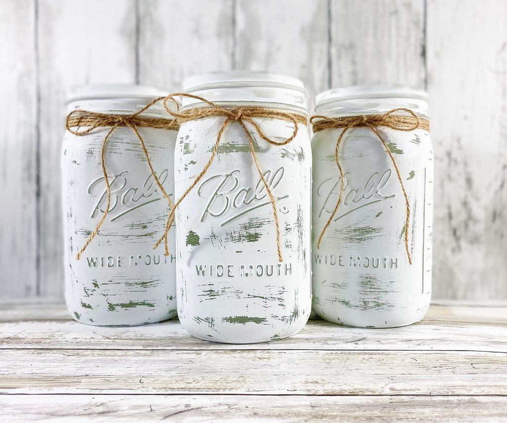 Three white distressed mason jars with mixed greenery and white blooms overhead angle