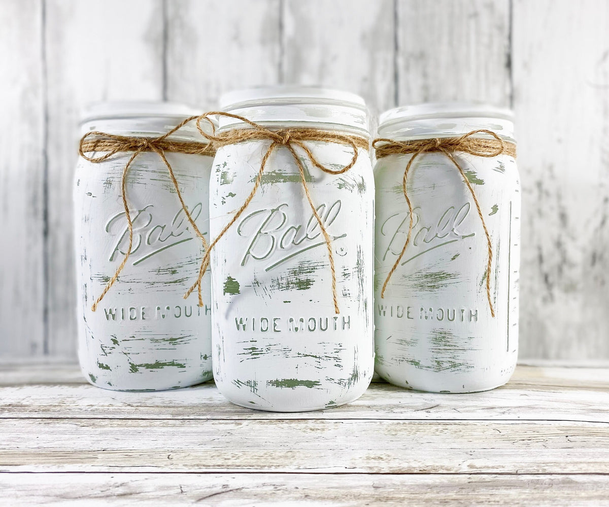 Three white distressed mason jars with mixed greenery and white blooms overhead angle