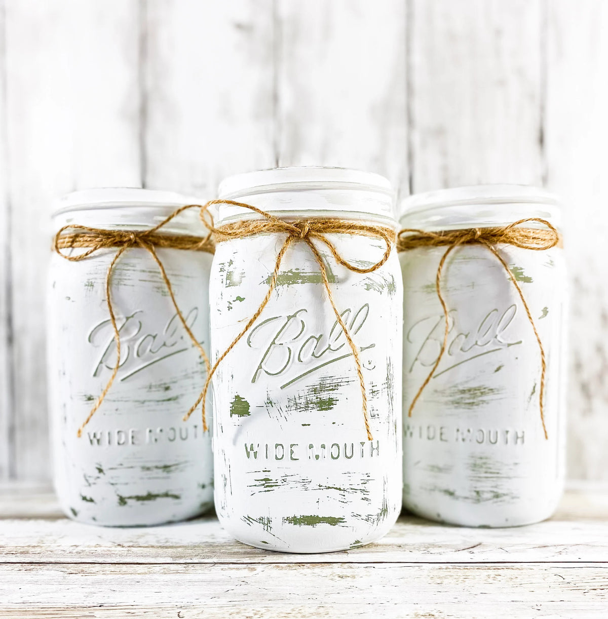 Single white painted Ball mason jar with jute bow on wood table with staircase background