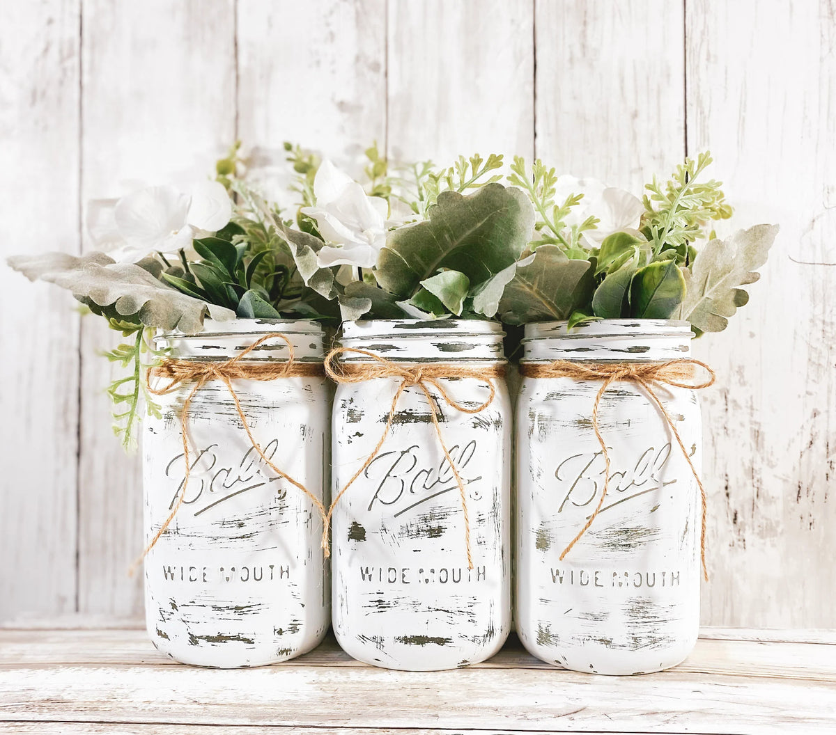 Set of 3 white mason jars with white hydrangeas and mixed greenery on white background