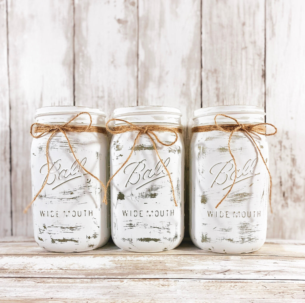 Three white distressed mason jars with eucalyptus and white flowers front angle