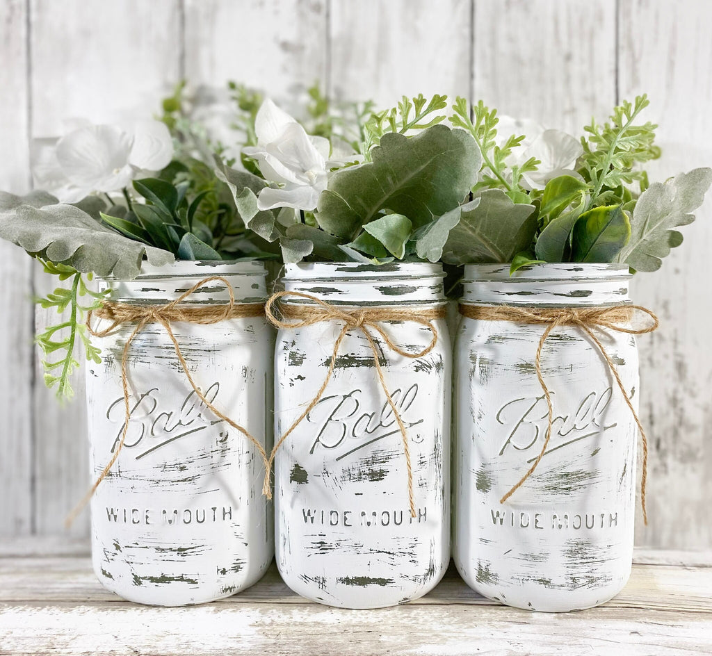 White painted Ball mason jars with greenery and white flowers on white shiplap
