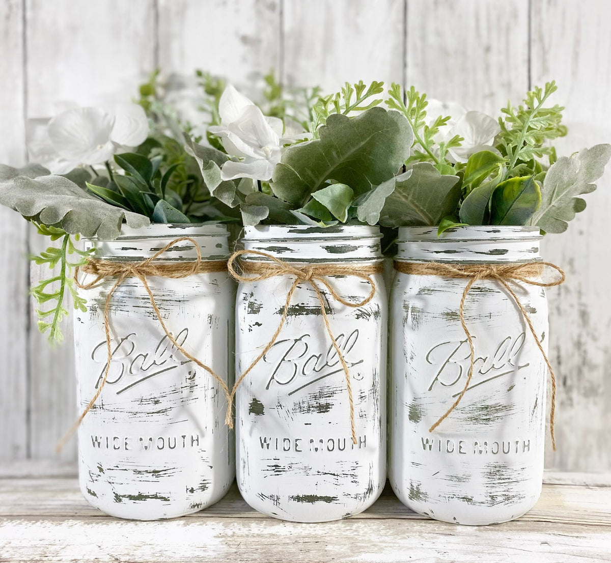 White painted Ball mason jars with greenery and white flowers on white shiplap