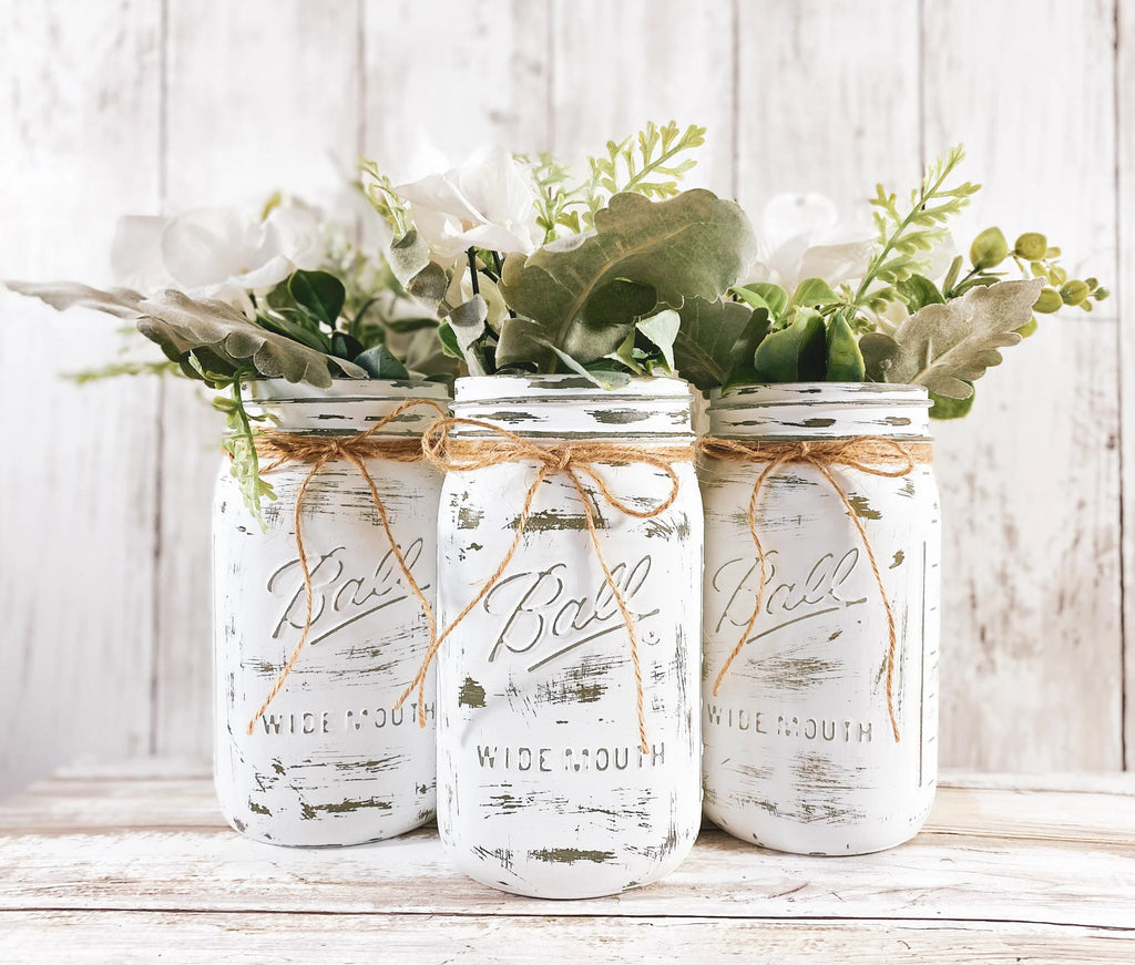 Set of 3 white distressed Ball mason jars with eucalyptus and white flowers on white wood