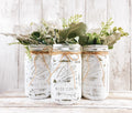 Set of 3 white distressed Ball mason jars with eucalyptus and white flowers on white wood