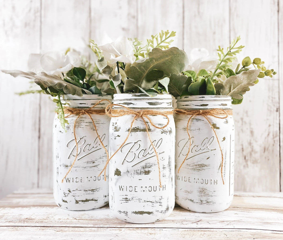 Set of 3 white distressed Ball mason jars with eucalyptus and white flowers on white wood