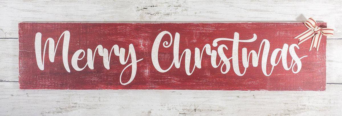 Merry Christmas farmhouse wood sign distressed cranberry red with white script lettering and red white striped bow resting on pine garland with red and silver ornaments below on white shiplap