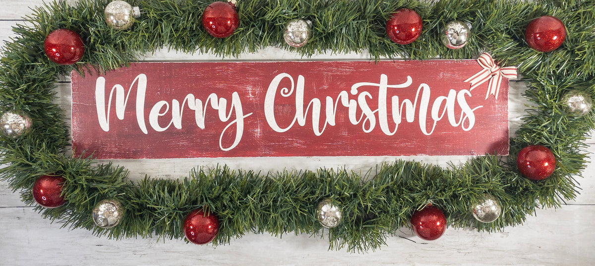 Merry Christmas farmhouse wood sign distressed cranberry red with white script lettering and red white striped bow on white shiplap wall wide shot