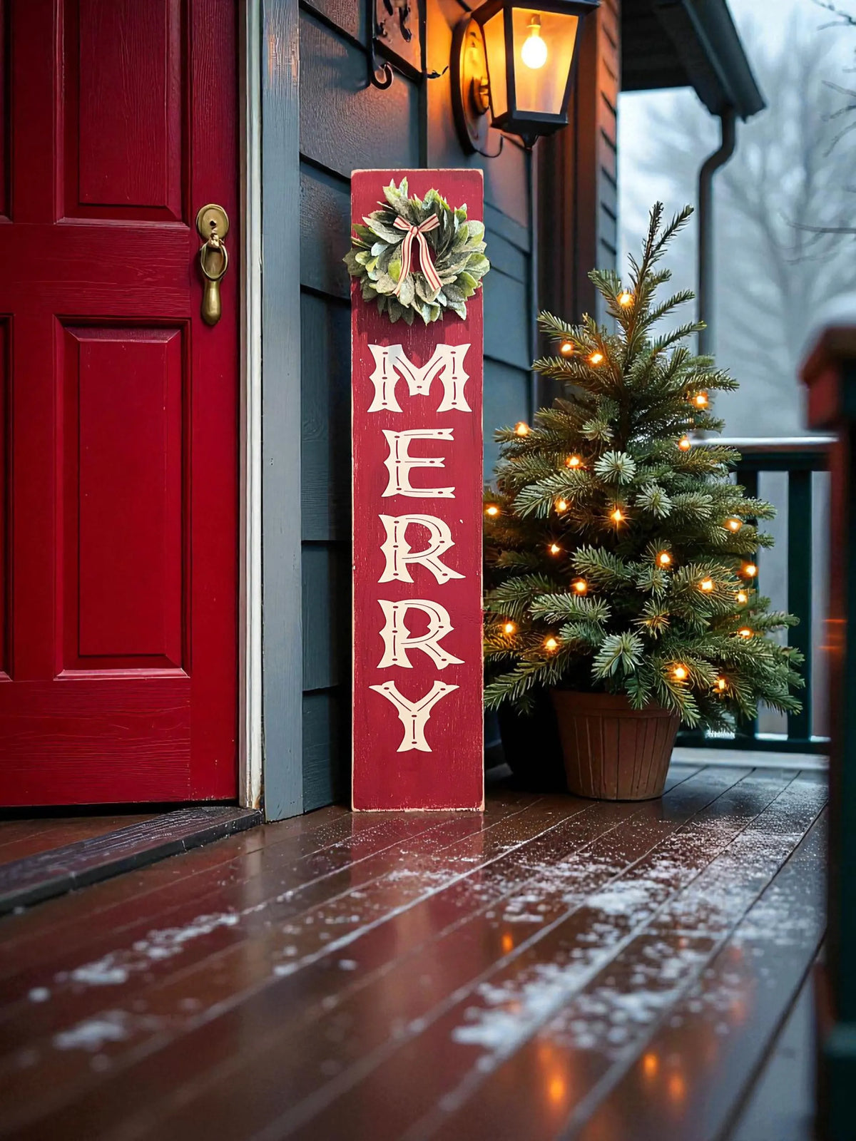 MERRY porch leaner sign with holly wreath leaning against gray front door with Christmas garland and lit Christmas tree