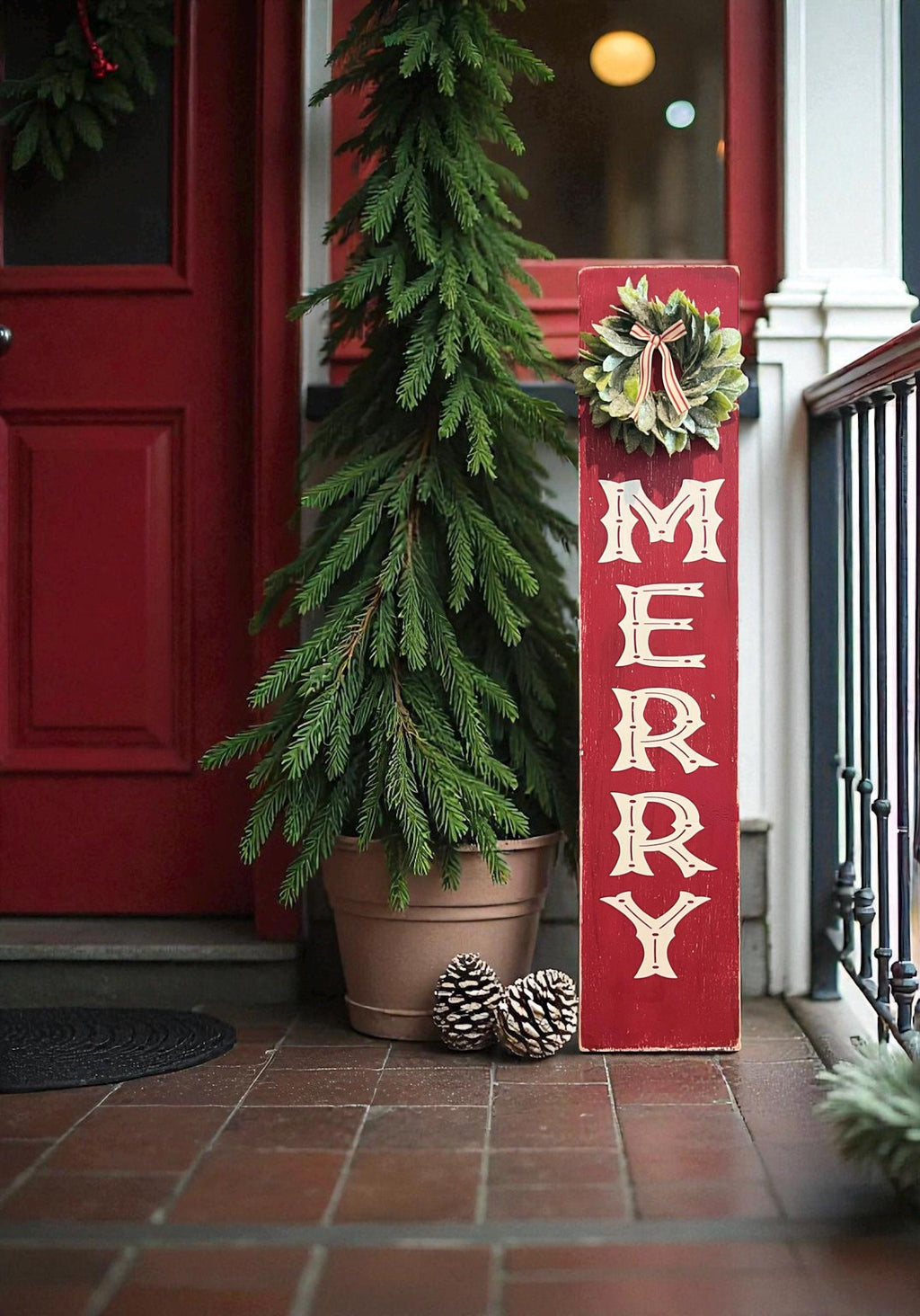 MERRY porch leaner sign with holly wreath leaning against dark red front door with snowy porch and lit Christmas tree