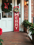 MERRY porch leaner sign with holly wreath leaning against red front door with Christmas greenery and lanterns