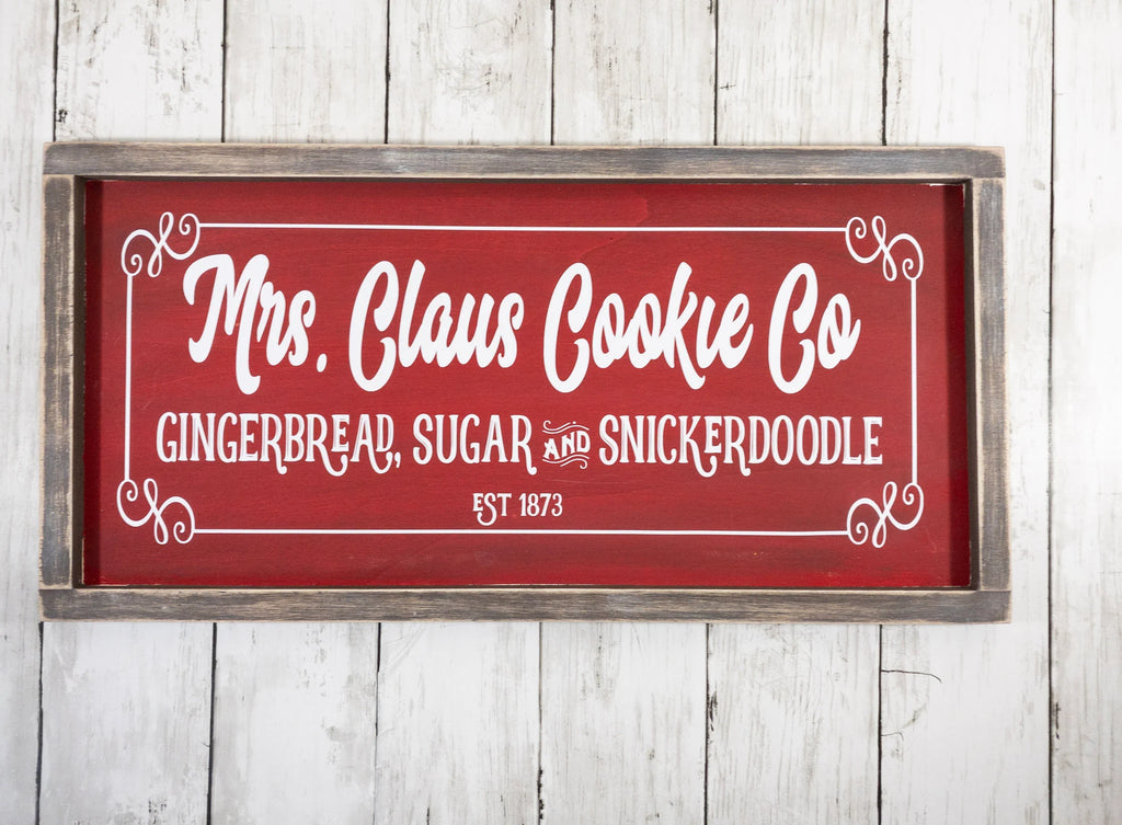 Mrs Claus Cookie Co framed Christmas sign crimson red with white script and serif lettering in distressed gray wood frame on white shiplap wall hero shot