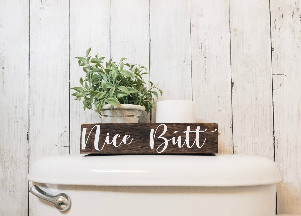 Nice Butt dark stained farmhouse toilet paper box on white surface with plant and toilet paper roll styled view