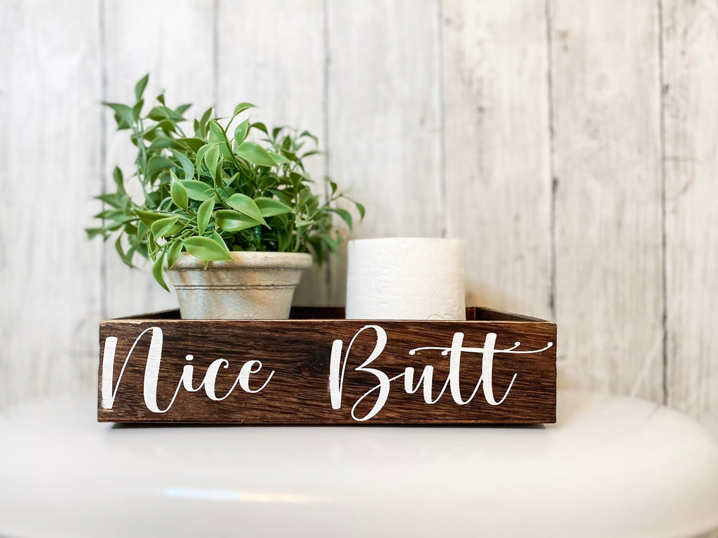 Nice Butt dark stained farmhouse toilet paper box on toilet tank with plant and toilet paper roll wide view