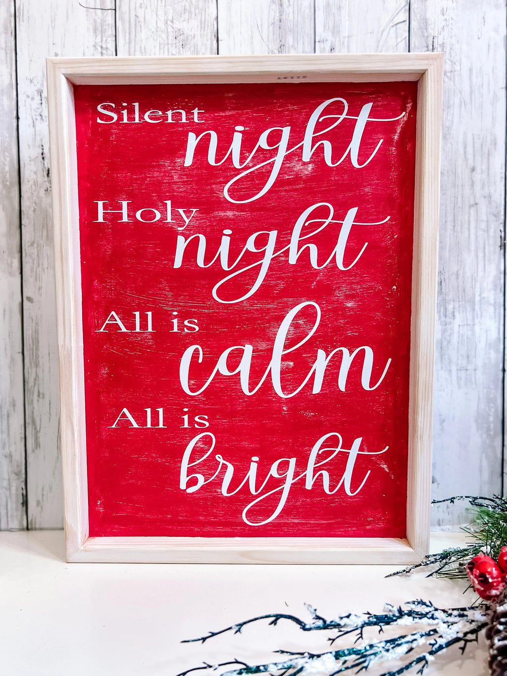 Red Silent Night Holy Night All is Calm All is Bright framed wood sign with whitewashed birch frame leaning against white shiplap wall with red berry pine cone spray close up