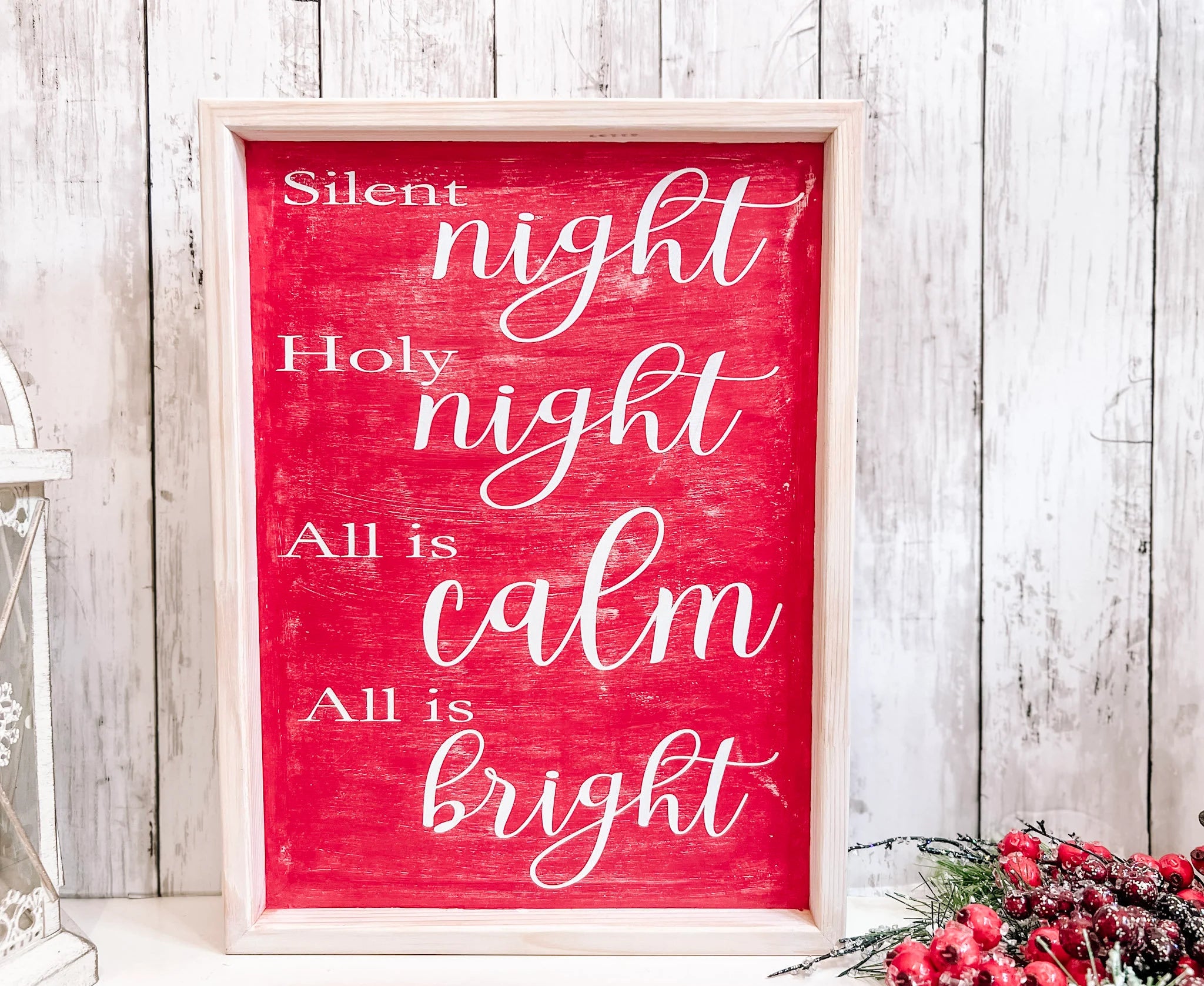 Red Silent Night Holy Night All is Calm All is Bright framed wood sign with whitewashed birch frame leaning against white shiplap wall with white lantern and red berry pine cone spray hero shot