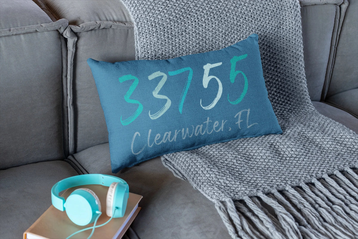 Personalized 33755 Clearwater FL navy lumbar pillow on leather sofa with rust throw pillow and woven blanket lifestyle shot
