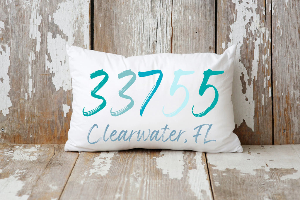 Personalized zip code lumbar pillow reading 33755 Clearwater FL in coastal teal blues on cream tufted sofa lifestyle shot