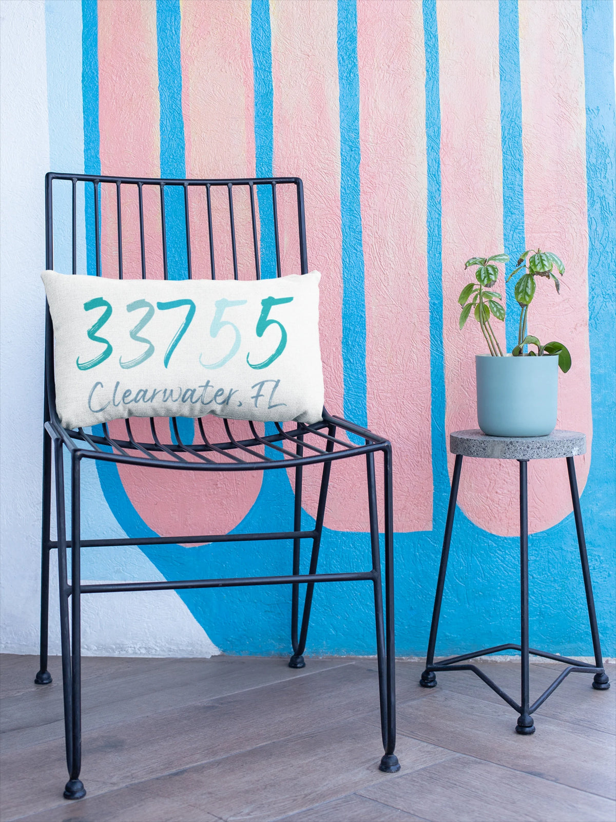 Personalized zip code lumbar pillow reading 33755 Clearwater FL in coastal teal blues on rustic wood surface with galvanized milk jug