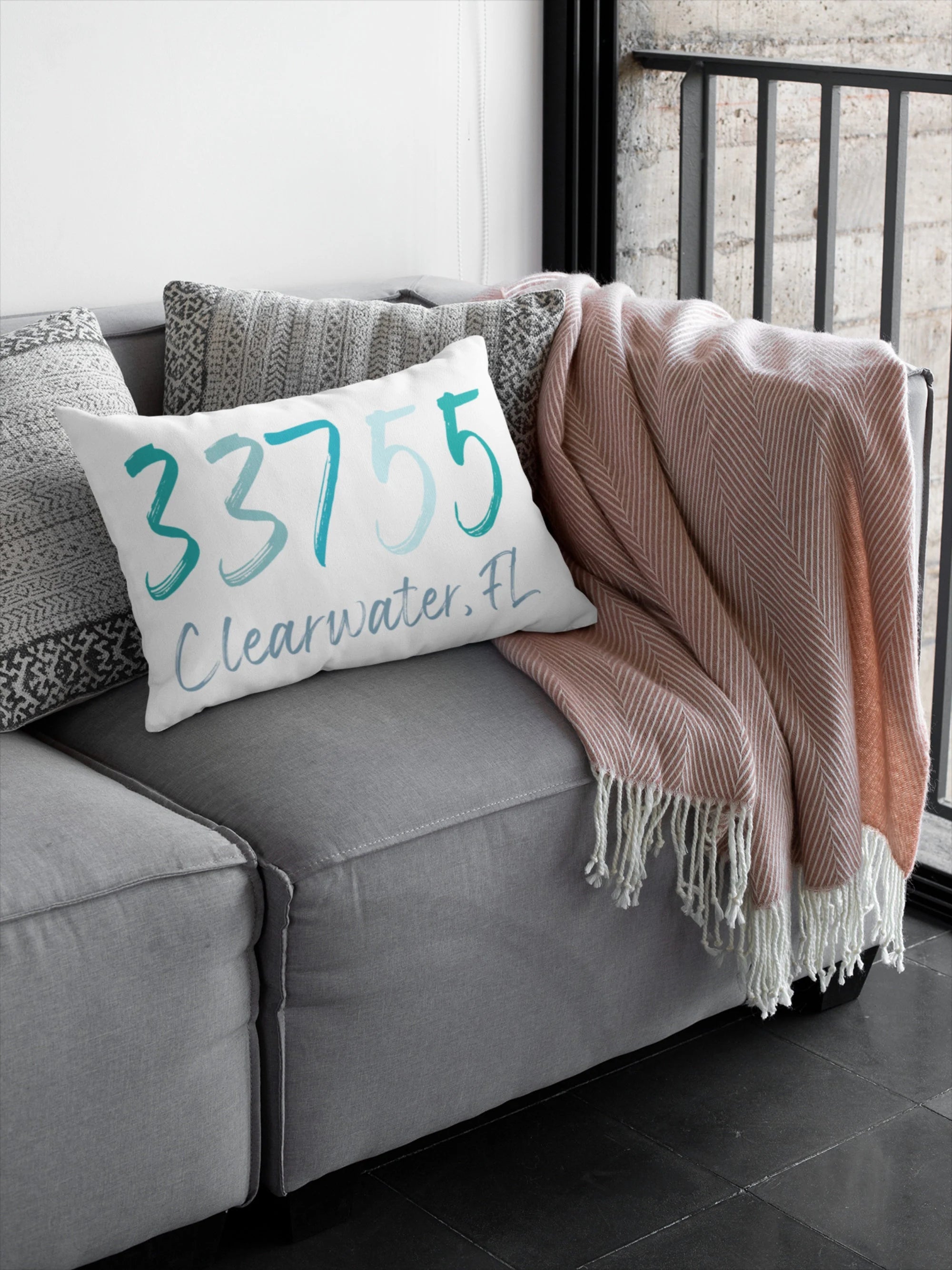 Personalized zip code lumbar pillow reading 33755 Clearwater FL in coastal teal blues on black wire chair against colorful striped wall