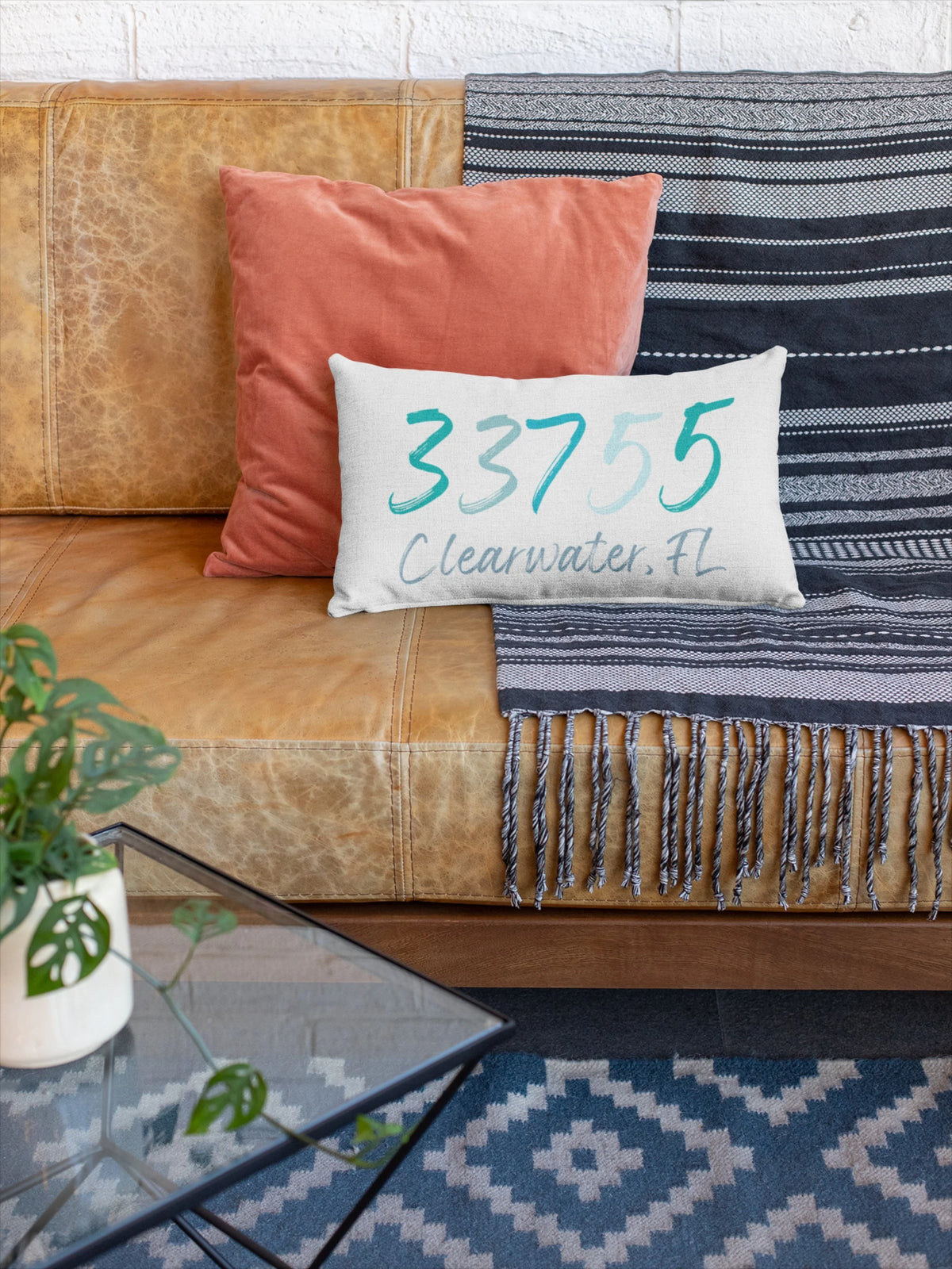 Personalized zip code lumbar pillow reading 33755 Clearwater FL in coastal teal blues on cream tufted sofa with gray knit blanket