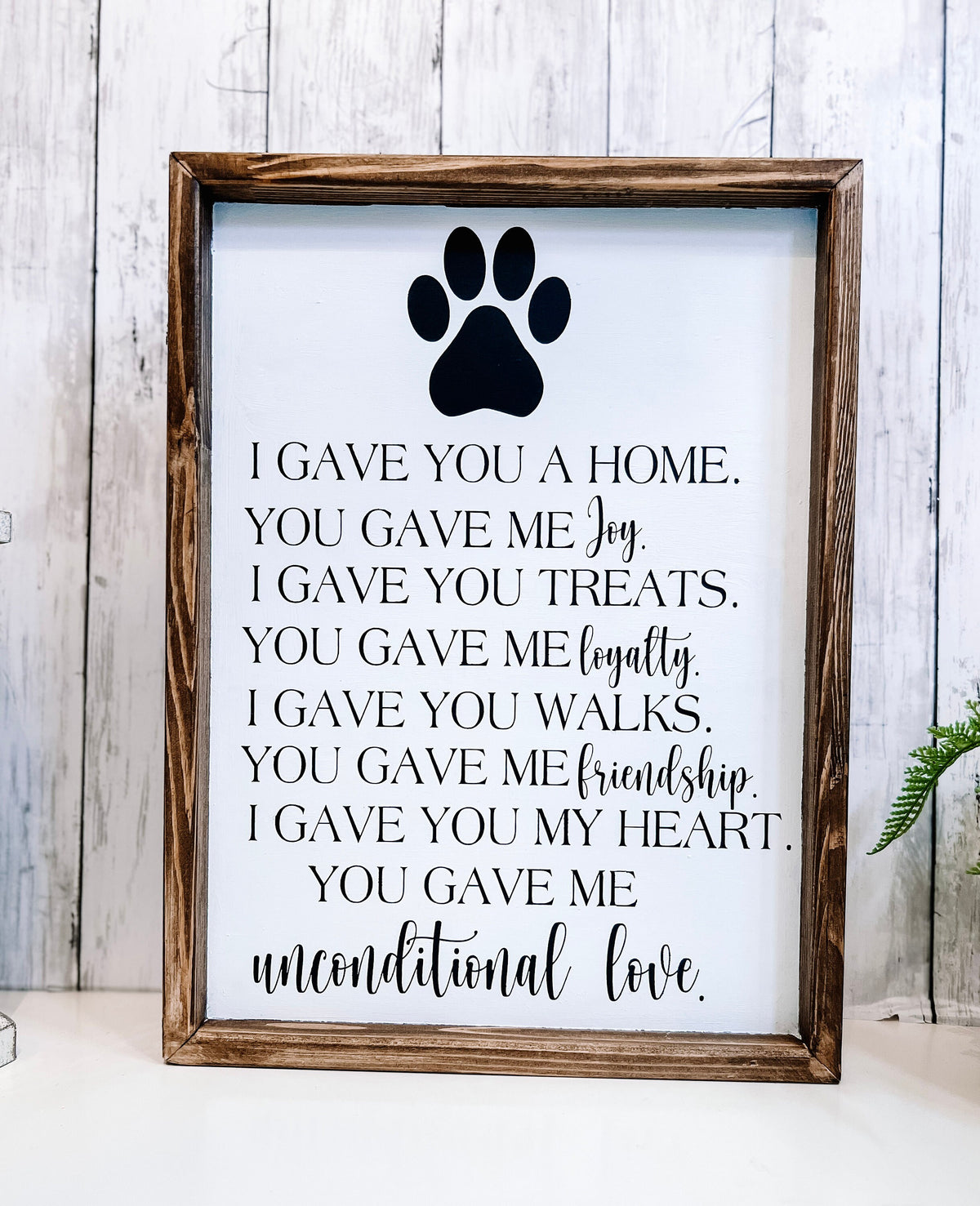 Personalized pet memorial sign with black paw print front view on white surface with green plant