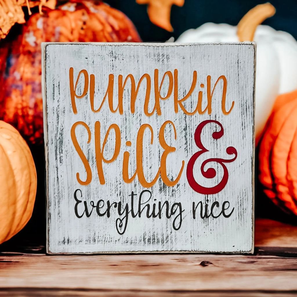 Pumpkin Spice and Everything Nice distressed whitewash wood block sign with amber script orange serif and burgundy ampersand on rustic wood surface with pumpkin spice latte and orange pumpkin