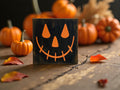 Jack-o-lantern black wood block sign with orange face on white wood porch with large orange pumpkins and fall leaves