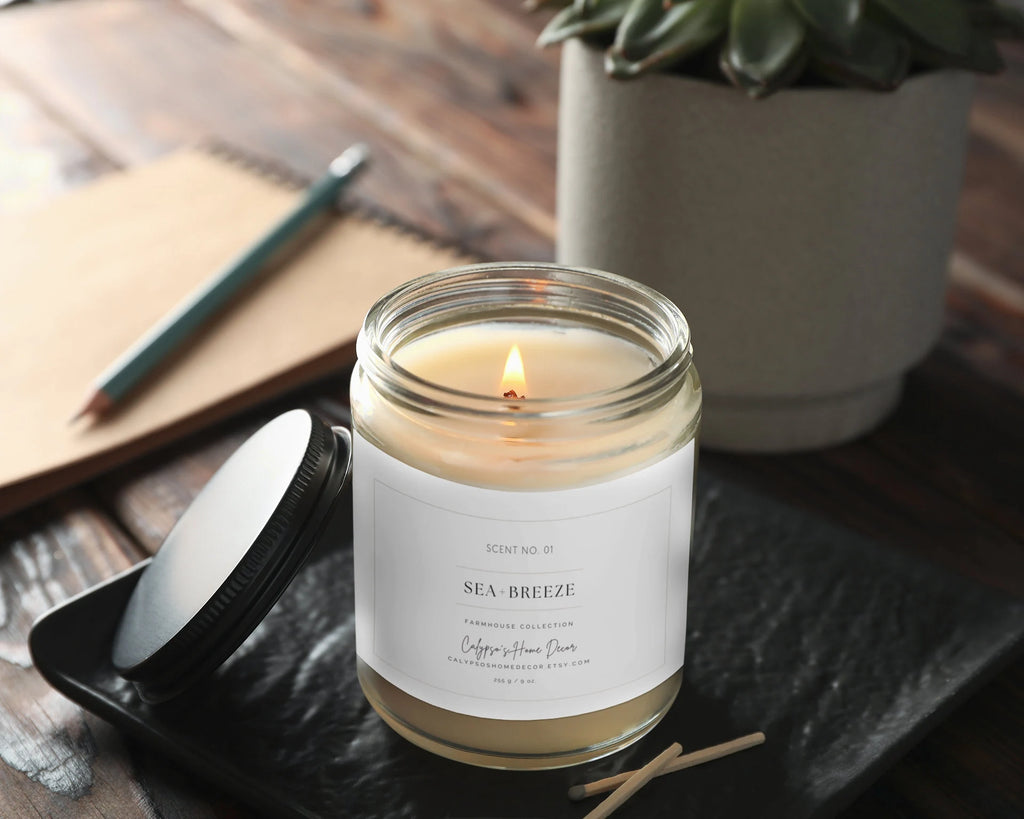 Sea Breeze candle lit on marble surface with essential oil bottles and tropical plant in background