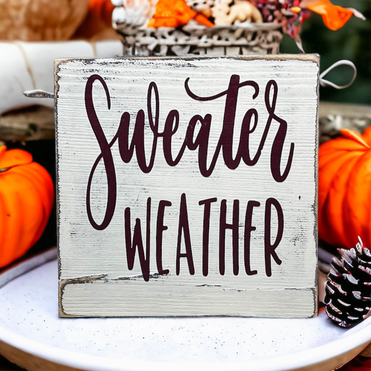 Sweater Weather sign close up with fall foliage background