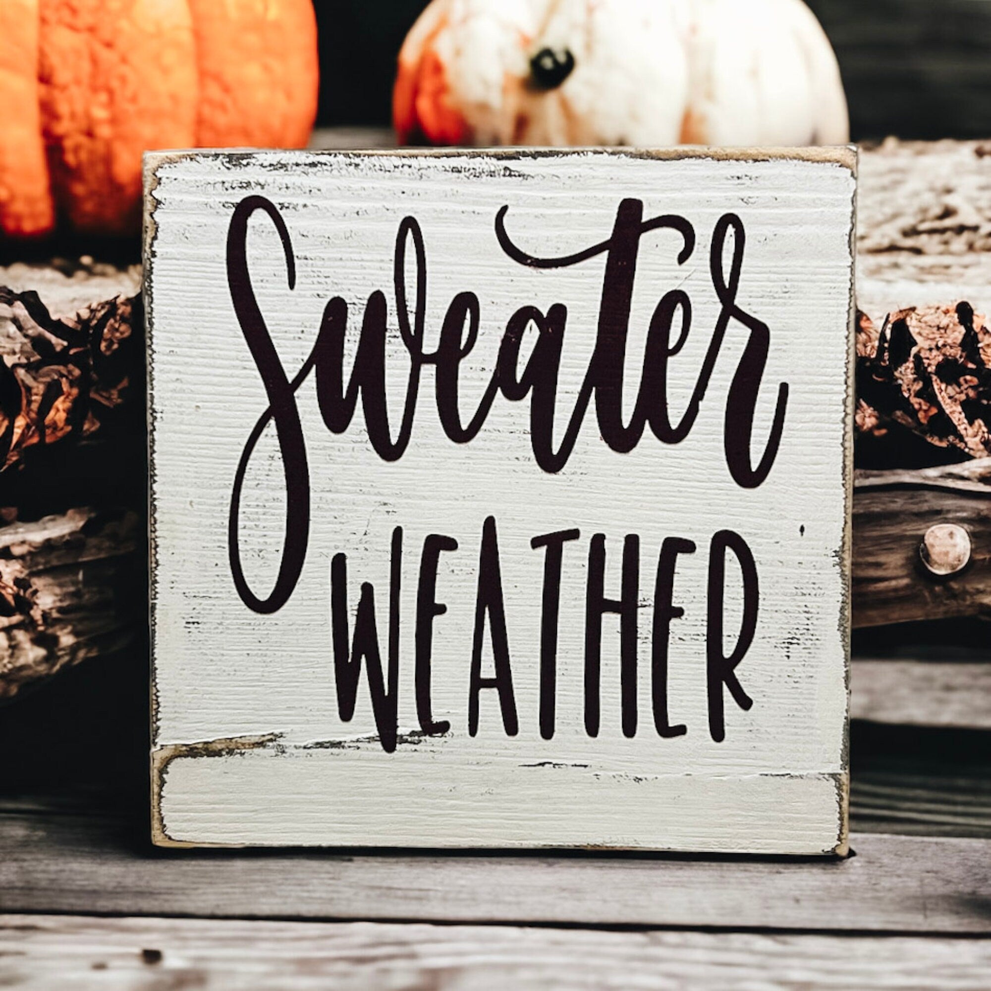 Sweater Weather sign on wood surface with orange pinecone and pumpkin