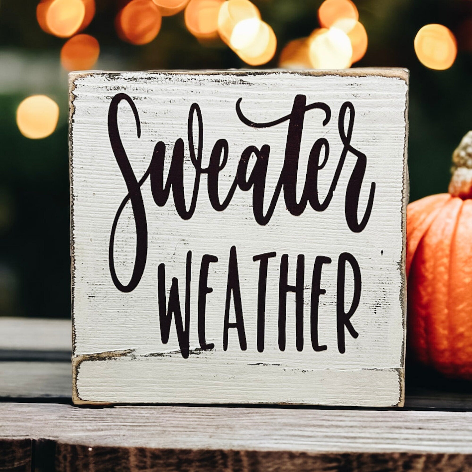 Sweater Weather sign on weathered wood with pumpkin and red pinecone