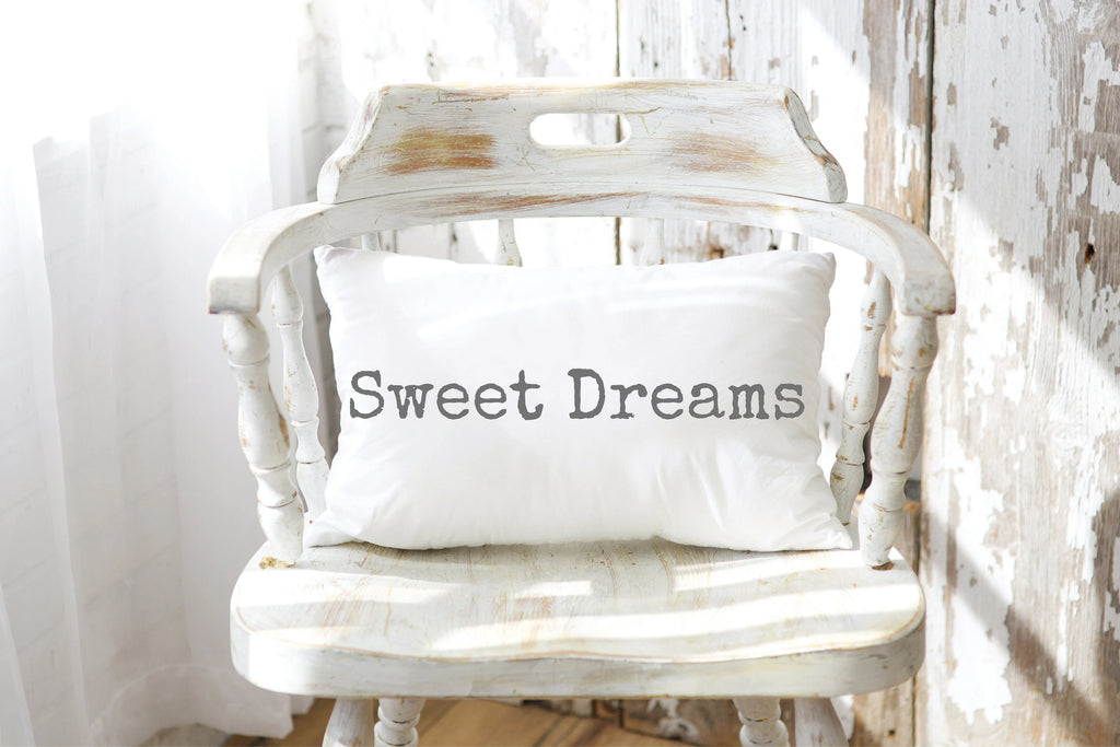 Sweet Dreams white lumbar pillow with gray distressed typewriter lettering leaning against peeling white barn wood wall on rustic wood floor with vintage galvanized milk jug wide shot
