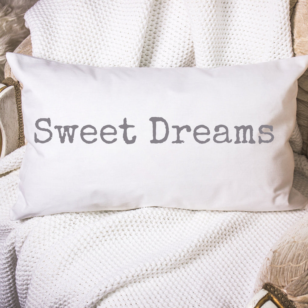 Sweet Dreams white lumbar pillow with gray distressed typewriter lettering on white knit throw blanket in wicker basket lifestyle shot wide