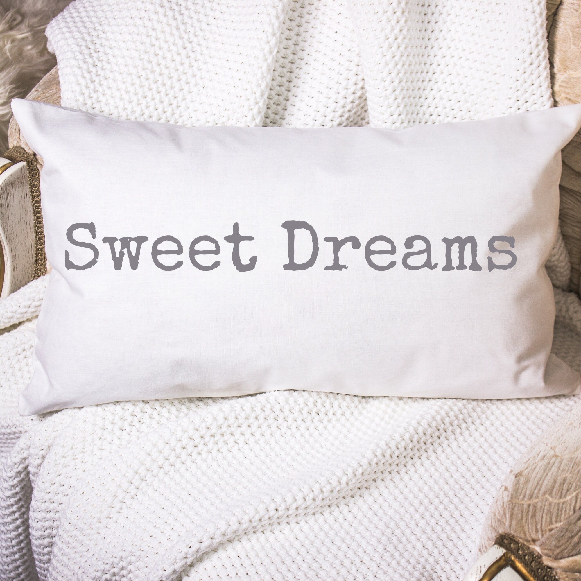 Sweet Dreams white lumbar pillow with gray distressed typewriter lettering on white knit throw blanket in wicker basket lifestyle shot wide