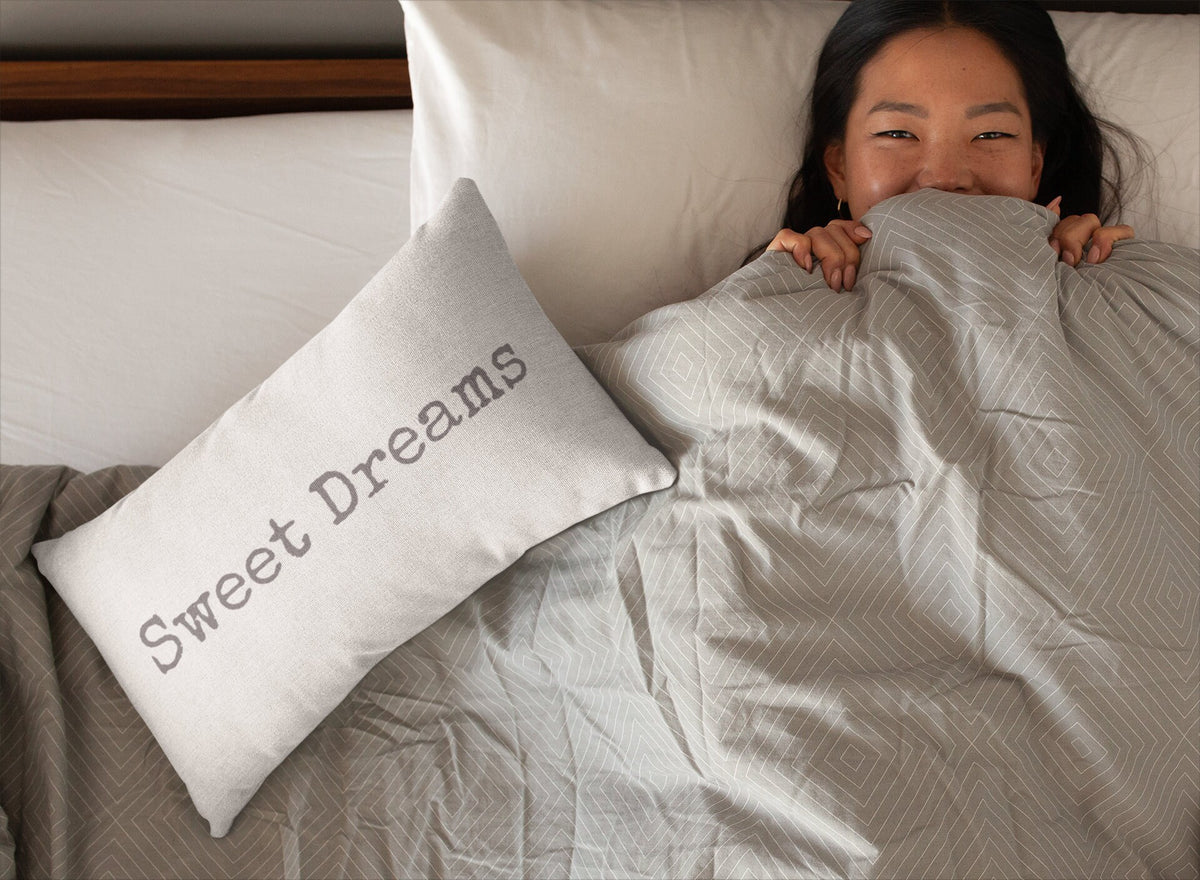 Sweet Dreams white lumbar pillow with gray distressed typewriter lettering leaning against peeling white barn wood wall on rustic wood floor with vintage galvanized milk jug lifestyle shot