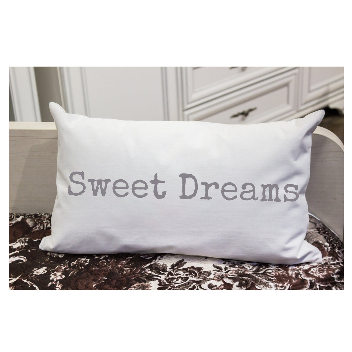 Sweet Dreams white lumbar pillow with gray distressed typewriter lettering on white distressed wood chair with sheer curtain window light lifestyle shot